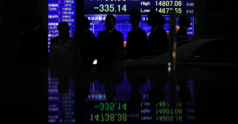 16.out.2014 - Pedestres na frente de um painel eletrônico mostrando o índice Nikkei, da Bolsa de Tóquio, são refletidos em uma superfície de pedra polida, na capital do Japão