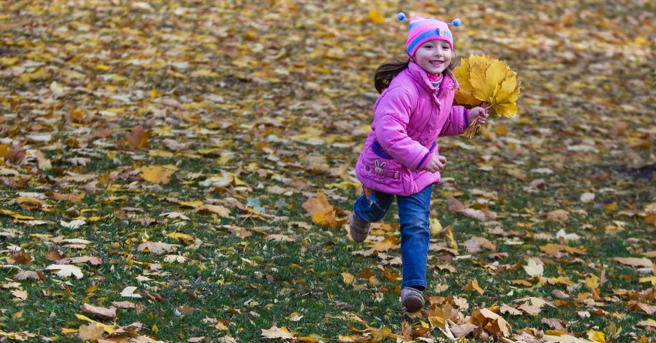 17.out.2014 - Menina corre com folhas de outono coletadas em um parque em Donetsk, na Ucrânia