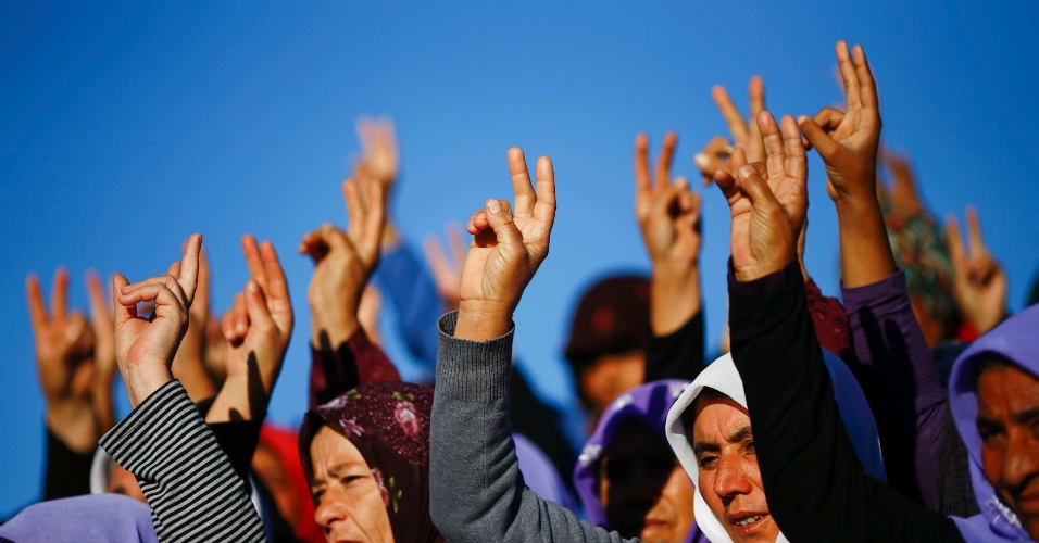 21.out.2014 - Mulheres fazem o sinal da vitória durante o funeral de combatentes curdos mortos em um cemitério na cidade de Suruc, na Turquia. Eles morreram durante confrontos contra militantes do Estado Islâmico em Kobane