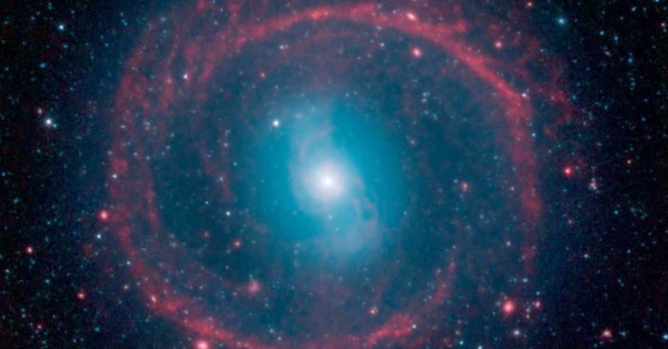 24.out.2014 - Imagem obtida pelo telescópio infravermelho Spitzer, da Nasa (agência espacial americana), mostra estrelas jovens e antigas em ação na galáxia NGC 1291, localizada na constelação de Erídano.  O anel externo, de cor vermelha, aparece repleto de novas estrelas que estão acendendo e aquecendo o pó. As estrelas na área central são mais velhas e tem cor azul, elas ficam localizadas nessa área, pois já utilizaram todo o gás disponível para criar novas estrelas. A galáxia é considerada ?barrada?, pois uma barreira de estrelas (que parece um S, na parte azul da imagem) domina seu centro