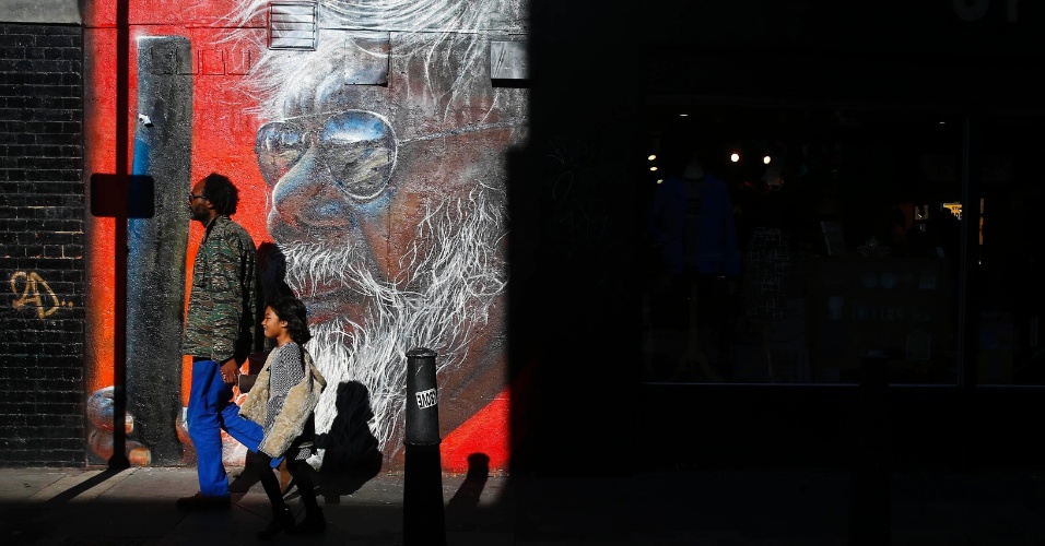 28.out.2014 - Um homem e uma criança a pé passam em frente a uma parede pintada com uma arte de rua e iluminada pelo sol em Shoreditch, em Londres, na Inglaterra
