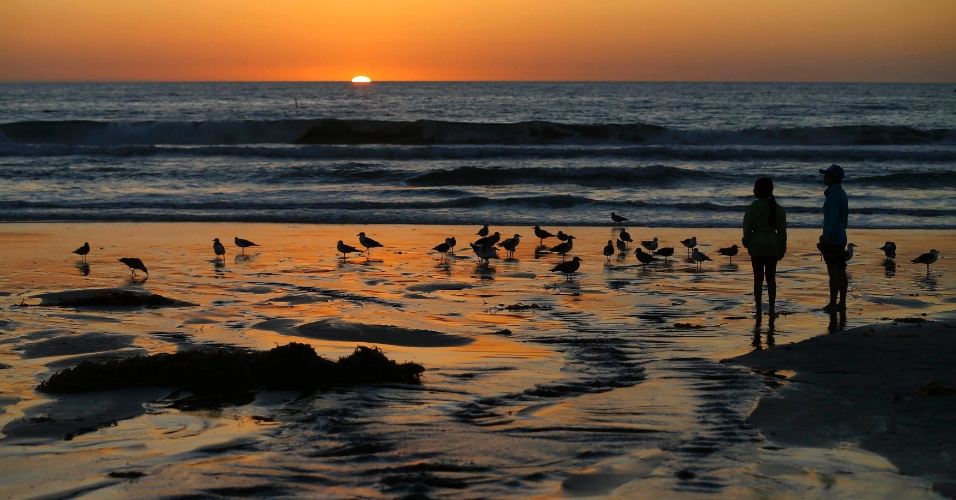 29.out.2014 - Crianças olham para as aves ao  pôr do sol na praia de Moon Light, em Encinitas, na Califórnia, nos EUA