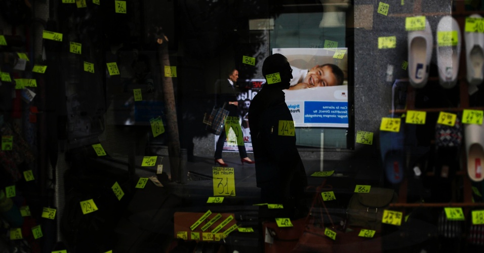 30.out.2014 - Pessoas são refletidas na vitrine de uma loja de calçados e bolsas no centro de Madri, na Espanha