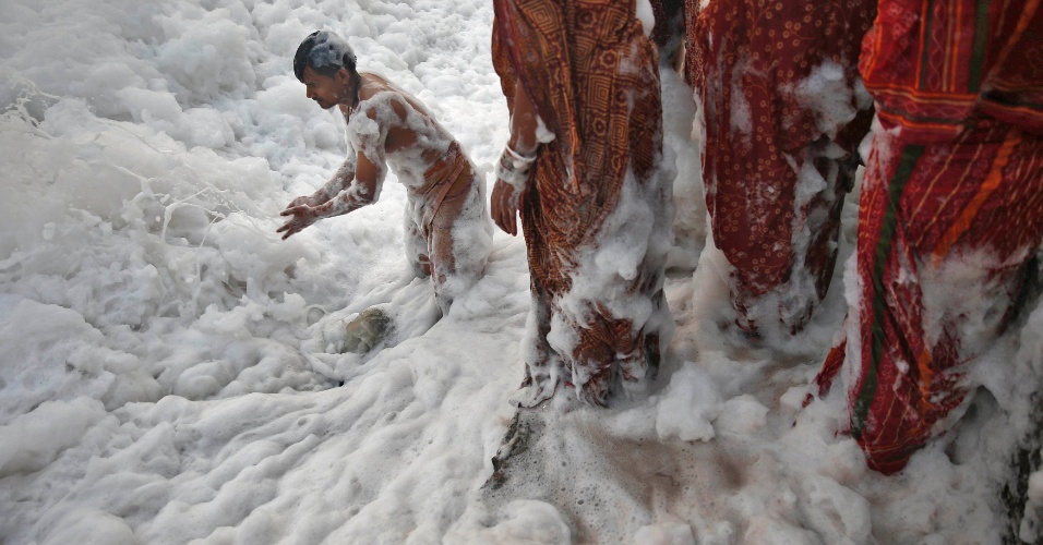 30.out.2014 - Devoto hindu empurra a espuma para liberar espaço para outros devotos adorarem o deus sol Surya nas águas poluídas do rio Yamuna durante festival religioso em Nova Déli, na Índia