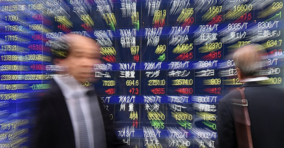 11.nov.2014 - Executivos passam em frente a um painel eletrônico com cotações das ações em Tóquio, no Japão