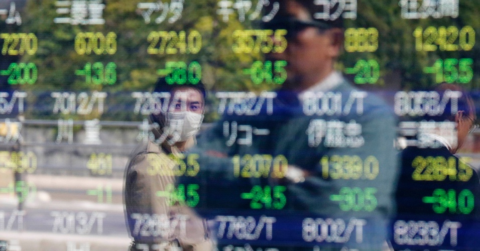 17.nov.2014 - Pessoas são refletidas em uma painel eletrônico de cotação de ações de uma corretora em Tóquio, no Japão