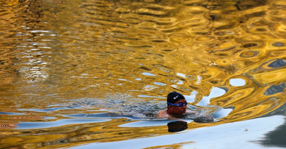 18.nov.2014 - Um homem nada nas águas de um canal onde as folhas amarelas das árvores aparecem refletidas em Pequim, na China