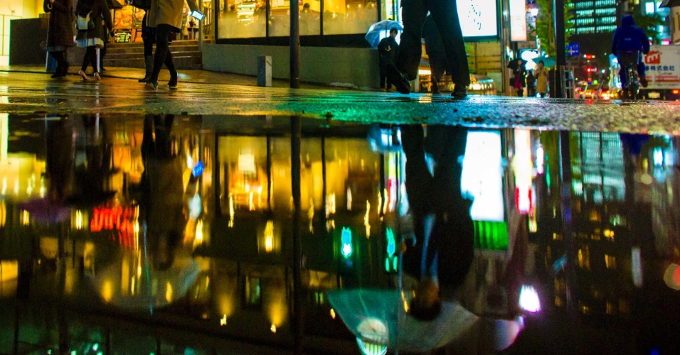 25.nov.2014 - Reflexo de pessoas que atravessaram uma rua no distrito de negócios apareceu em uma poça d'água nesta terça-feira (25), um dia chuvoso no centro de Tóquio, no Japão