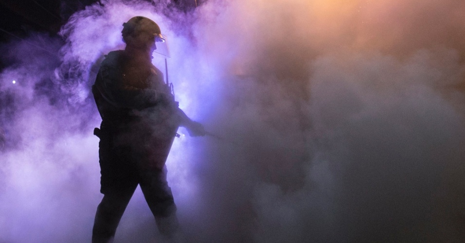 26.nov.2014 - Policial tentou apagar o fogo de uma viatura incendiada nesta terça-feira (25) por manifestantes em Ferguson, no Missouri, nos EUA