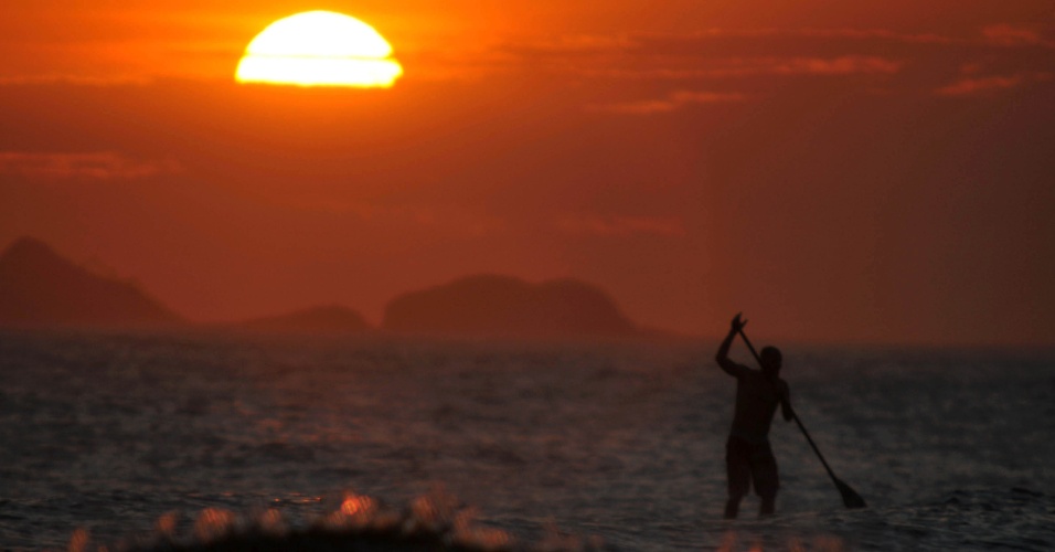 3.dez.2014 - Banhista faz stand up paddle na praia de Ipanema, enquanto o sol se põe na zona sul do Rio de Janeiro