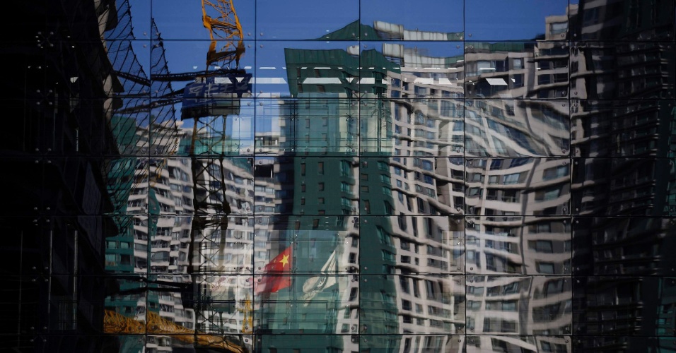 15.dez.2014 - Um canteiro de obras e um edifício residencial são refletidos na parede de vidro de um prédio em Pequim, na China