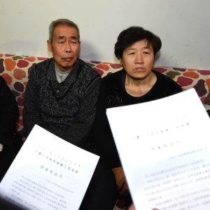 Li Sanren (à esq.) e Shang Aiyun, pais de Huugjilt, recebem documento legal sobre o novo processo nesta segunda-feira (15). O chinês foi considerado inocente 18 anos após ser sentenciado à morte, em 1996 - Ren Junchuan/Xinhua