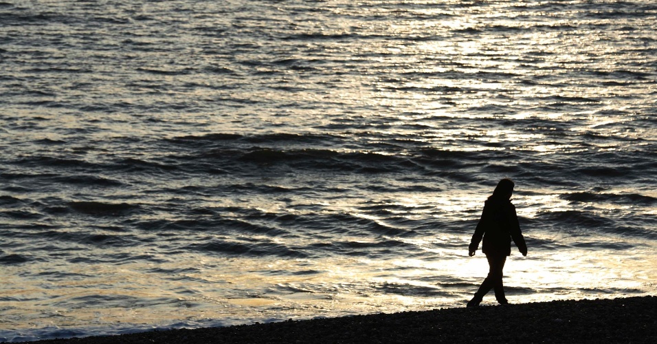 16.dez.2014 - Uma mulher anda por praia com o sol se pondo em Brighton, na Inglaterra