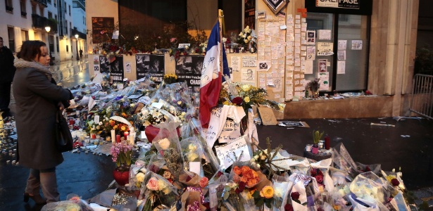 Mulher olha para as flores e outros objetos depositados na frente do prédio onde fica a redação da revista "Charlie Hebdo", em Paris - Jacques Demarthon/AFP