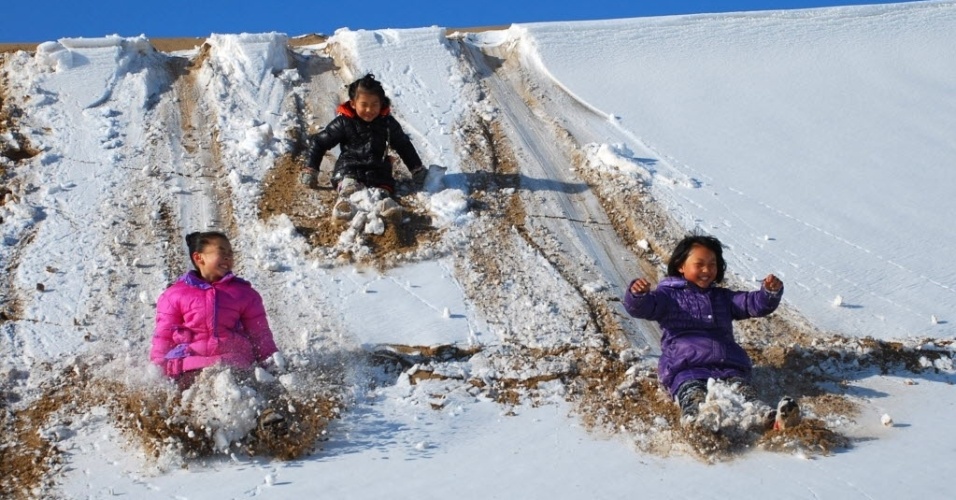 17.jan.2015 - Três jovens turistas deslizam em monte de neve que se formou em cima de dunas de areia na montanha Mingsha em Sunhuang. Na China
