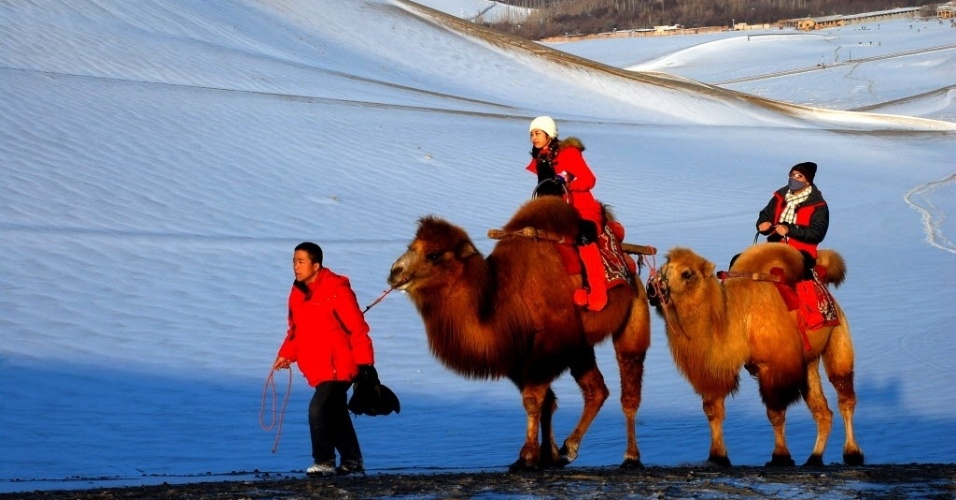 17.jan.2015 - Turistas andam de camelo em dunas de areia que foram cobertas por neve na montanha Mingsha, em Sunhuang, na China