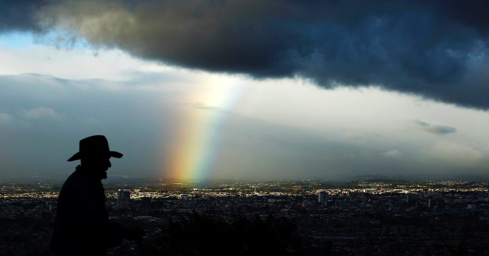 30.jan.2015 - Homem caminha com um arco-íris ao fundo, abaixo de nuvens escuras em San Jose, na Costa Rica
