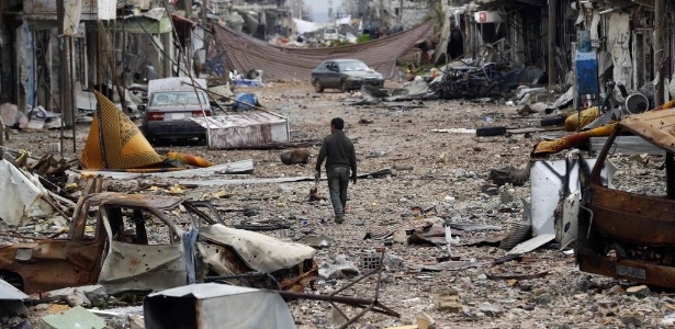 30.jan.2015 - Homem caminha nesta sexta-feira (30) por rua com carros abandonados e edifícios danificados em Kobani, um enclave curdo na Síria - Osman Orsal/Reuters