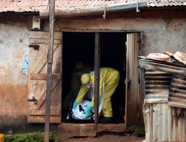Agentes da saúde da Cruz Vermelha de Serra Leoa responsáveis pelo enterro de vítimas do ebola retiram um corpo de uma casa em Freetown - Francisco Leong/AFP