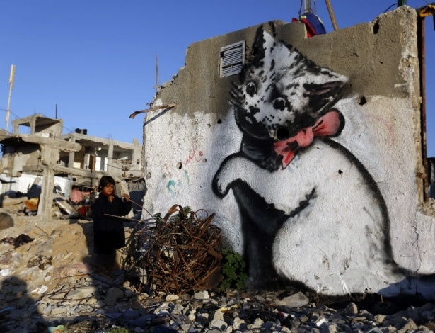 27.fev.2015 - Criança palestina para ao lado de um muro com uma pintura de gato, atribuída ao artista britânico Banksy, na faixa de Gaza