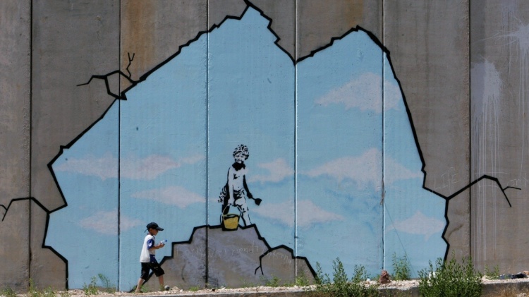 A Palestinian boy walks past one of Banksy's graffiti on the wall separating Israel from the West Bank - Ammar Awad/Reuters - Ammar Awad/Reuters