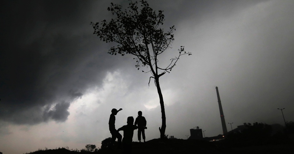 2.mar.2015 - Crianças em silhueta contra um fundo de nuvens de chuva, brincam nas margens do rio Yamuna, em Nova Déli, na Índia