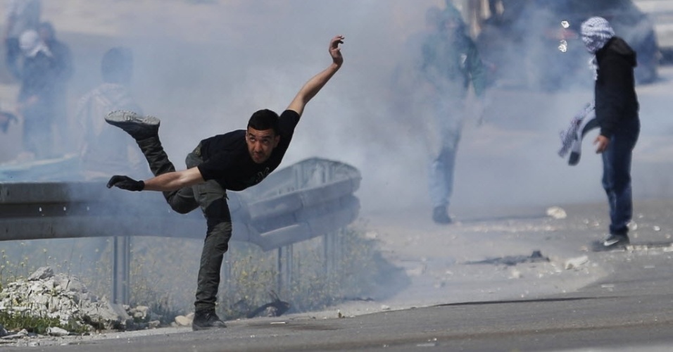 17.mar.2015 - Manifestante palestino joga de volta uma bomba de gás lacrimogêneo lançada por soldados israelenses durante um protesto contra o confisco de assentamentos judaicos, perto da cidade de Abu Dis, na Cisjordânia