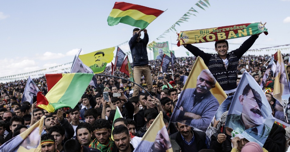 17.mar.2015 - Moradores da cidade turca de Suruc, na fronteira com a cidade síria de Kobani, acenam com bandeiras curdas e retrato do líder curdos Abdullah Ocalan preso durante celebração doNewroz, que marca a chegada da primavera e do novo ano nesta terça-feira (17)