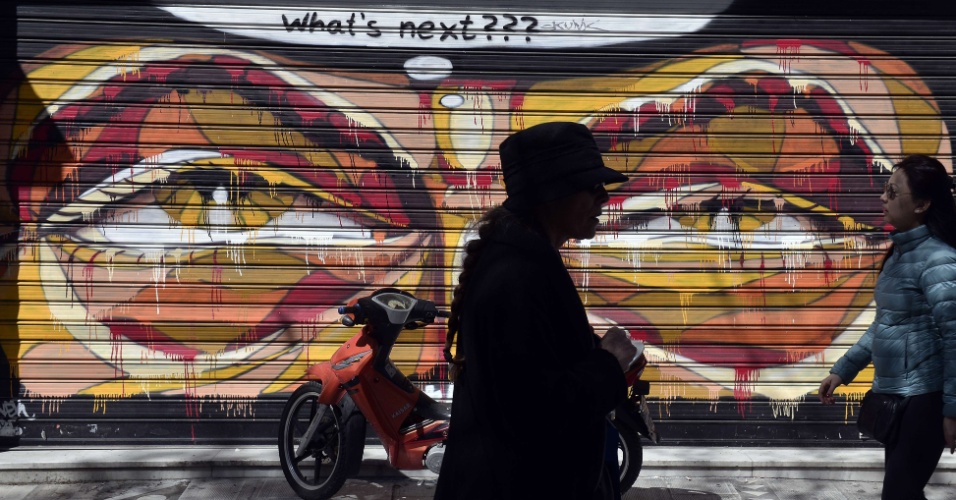 30.mar.2015 - Mulheres andam junto a um grafite feito na porta de uma loja fechada no centro de Atenas, na Grécia, onde se lê "Qual é o próximo", em tradução livre