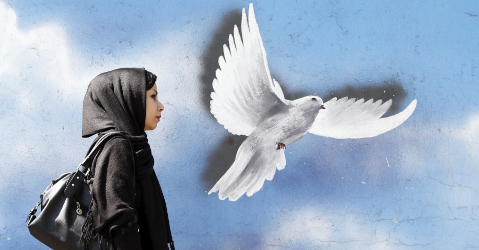 1º.abr.2015 - Mulher passa diante de muro com graffiti de uma pomba da paz, em Teerã (Irã)