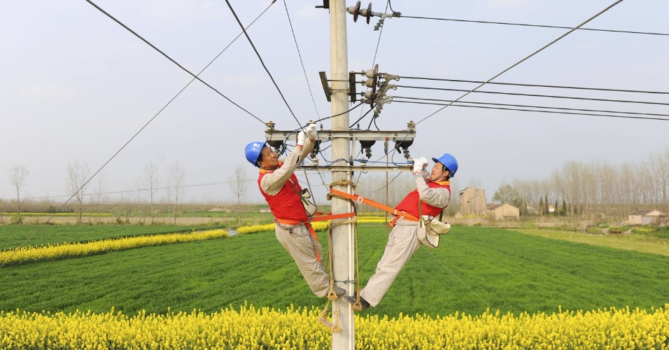 1º.abr.2015 - Técnicos trabalham na manutenção de um poste de eletricidade entre campos de cultivo em Chuzhou, na província de Anhui, na China