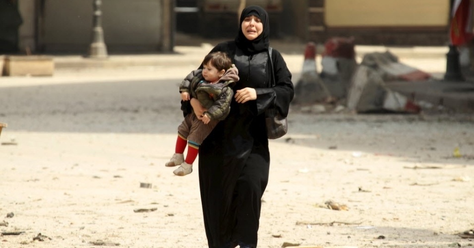 3.abr.2015 - Moradora carregando uma criança chora em local danificado por bombardeios provenientes das forças leais ao ditador da Síria, Bashar al Assad, em Idlib. Uma mesquita foi destruída no ataque, depois que os rebeldes tomaram o controle da área 