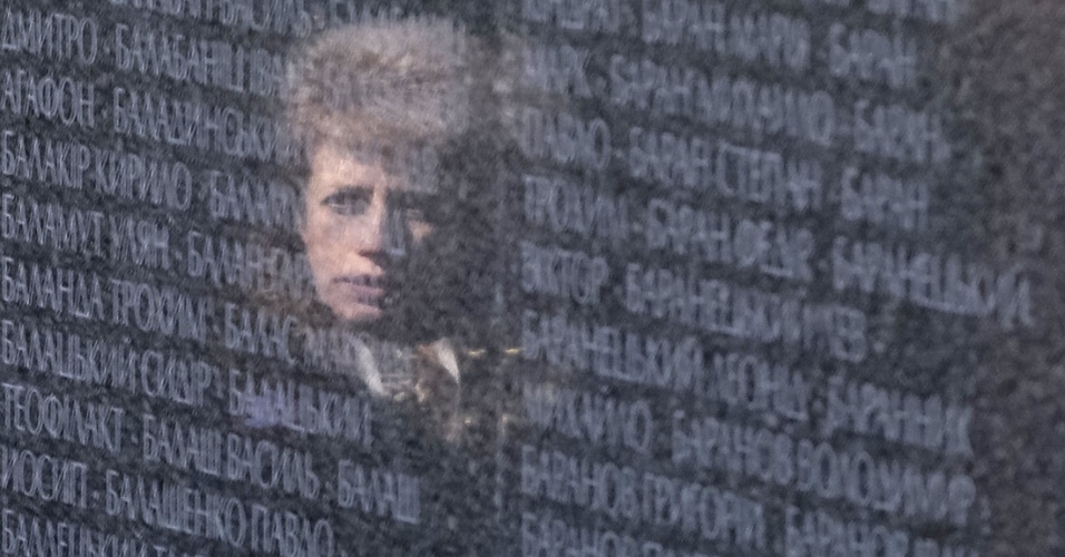 9.abr.2015 - Rosto de uma mulher é refletido em uma parede com os nomes das vítimas polonesas do ditador soviético Josef Stalin, durante cerimônia no memorial próximo à aldeia de Bykovnya, perto da capital Kiev, na Ucrânia