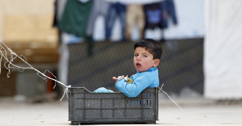 17.abr.2015 - Menino come enquanto brinca em uma cesta, dentro de campo para refugiados sírios, em Sidon, no Líbano