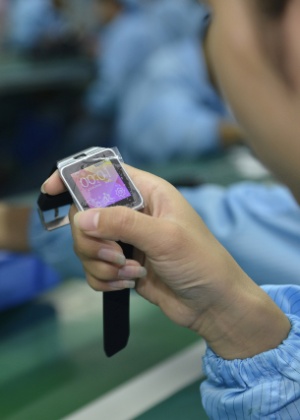 Trabalhadora chinesa analisa relógio inteligente em fábrica na cidade de Shenzen, na China. A proximidade do início das vendas do Apple Watch fez proliferar a produção de smartwatches genéricos - AFP