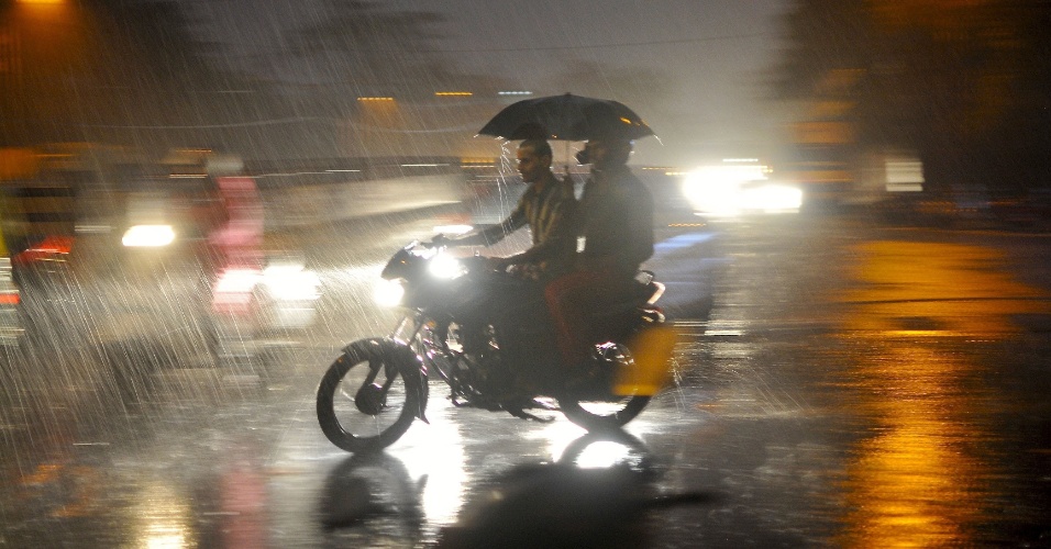24.abr.2015 - Homens atravessam estrada em meio a forte chuva em Bangalore, na Índia