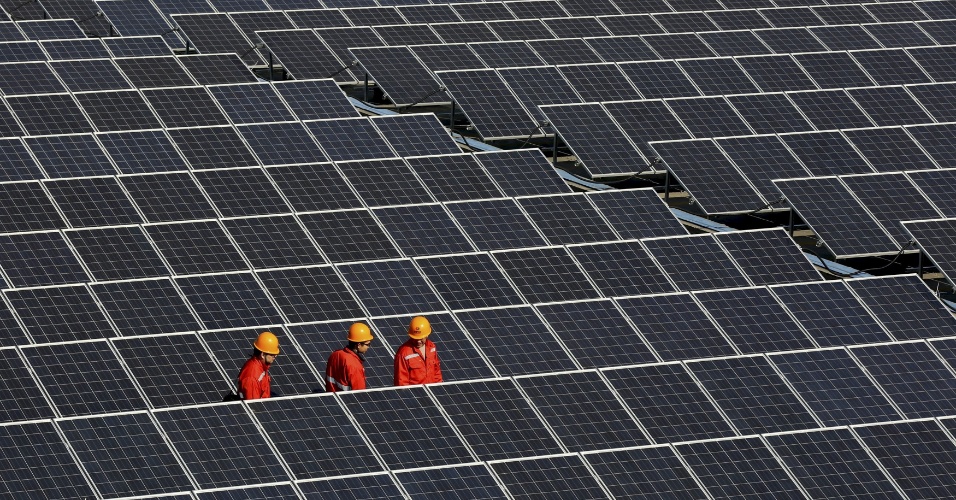 30.abr.2015 - Trabalhadores andam entre os painéis solares instalados recentemente em usina de energia solar em Zhouquan, província de Zhejiang, na China
