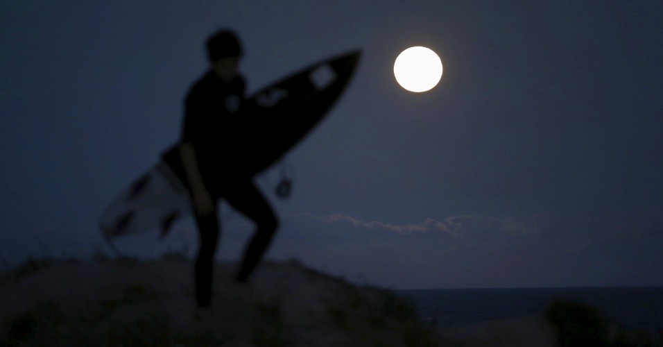 4.mai.2015 - Surfista caminha por dunas de areia na praia Wanda, em Sydney, Austrália, iluminada pela lua cheia 