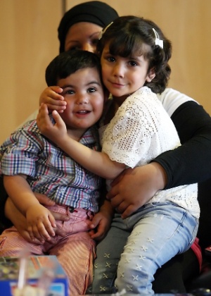 A menina síria Tala (dir) abraça o irmão, ambos sentados no colo da mãe, após reencontrá-los no aeroporto de Salônica, na Grécia