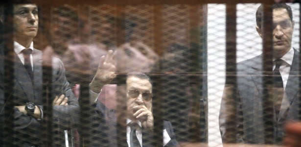 O ex-presidente egípcio acena desde a área destinada aos reús em tribunal no Cairo