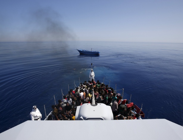 Grupo de cerca de 300 imigrantes africanos subsaarianos são alojados a bordo do navio da polícia italiana logo após abandonar o barco em que viajavam (em segundo plano, ao fundo) a deriva, na última quinta-feira (14), próximo à costa da Sicília - Alessandro Bianchi/Reuters