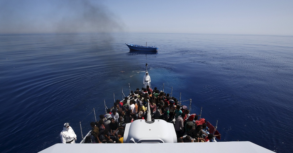 14.mai.2015 - Grupo de cerca de 300 imigrantes africanos subsaarianos são alojados a bordo do navio da polícia italiana logo após abandonar o barco em que viajavam (em segundo plano, ao fundo) a deriva, nesta quinta-feira (14), próximo à costa da Sicília. Ao todo, 1.100 imigrantes foram resgatados a 240 km de Lampedusa, segundo as autoridades