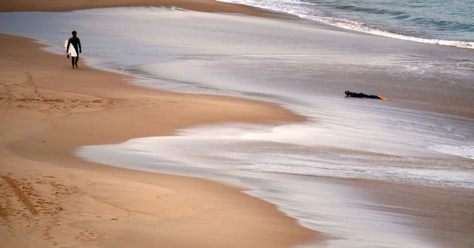 25.mai.2015 - Menino com roupas de mergulho descansa na areia da praia enquanto um surfista o observa na praia de Bondi de Sydney, na Austrália