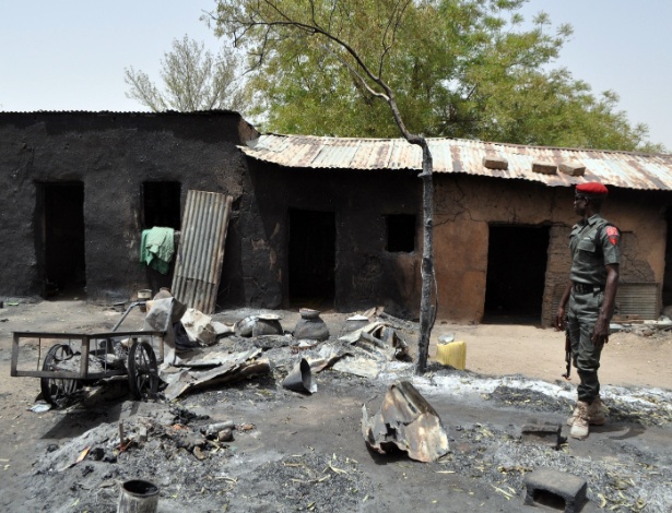 Polícia antiprotesto observa uma casa queimada em Gubio, no Estado de Borno, nordeste da Nigéria, durante ataque do Boko Haram - AFP
