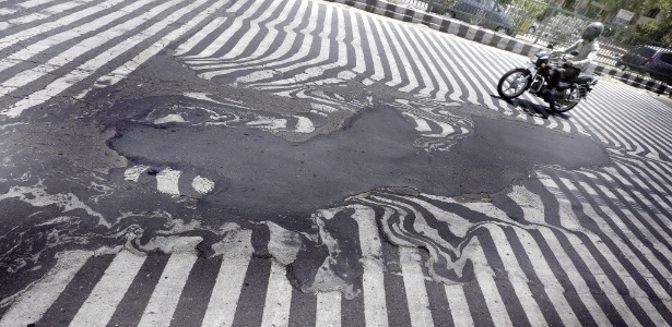  Motociclista passa perto de asfalto que derreteu por causa das altas temperaturas em Nova Déli, na Índia - Harish Tyagi/EPA