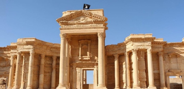 Imagem divulgada pelo meio de comunicação jihadista Welayat Homs em maio deste ano mostra uma bandeira do Estado Islâmico tremulando no alto da parede de um teatro romano de Palmira, na Síria. As ruínas da cidade estão na lista do Patrimônio da Humanidade da Unesco - AFP