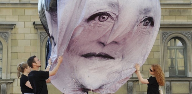 Ativistas da organização "One" de defesa do desenvolvimento inflam balão com a imagem do rosto de Merkel durante protesto na sexta (5) - Tobias Hase/Efe