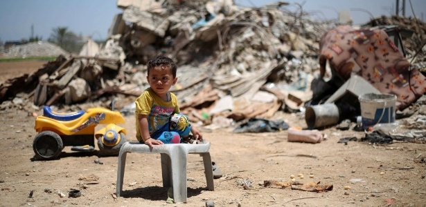 Criança palestina se senta na frente dos escombros de edifícios que foram destruídos durante a guerra de 50 dias entre Israel e o Hamas, entre julho e agosto de 2014, na aldeia de Khuzaa, a leste de Khan Yunis, no sul da faixa de Gaza. Israel bloqueou uma visita de enviado da ONU aos territórios palestinos pouco antes da publicação de um relatório sobre o conflito - Said Khatib/AFP