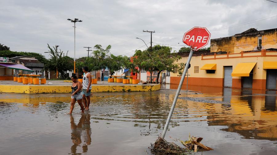 27.dez.2021 - Pessoas caminham na água em uma rua perto de uma placa de "Pare" de trânsito durante enchentes causadas por fortes chuvas em Itajuípe, na Bahia - Amanda Perobelli/Reuters