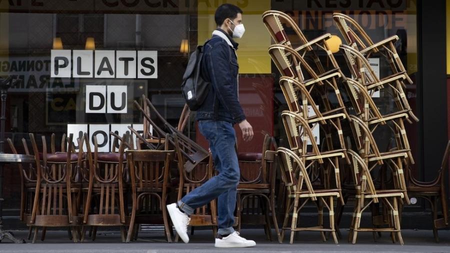 Homem caminha em frente a café fechado com as cadeiras empilhadas em Paris - EPA